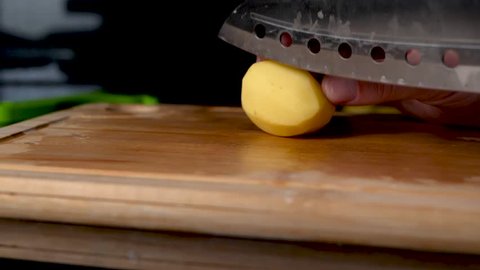 Close up shot of a silver knife chopping a potatoe, camera slides.