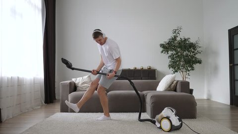Man Playing Virtual Guitar With Vacuum Cleaner Dancing At Home Wearing Headphones