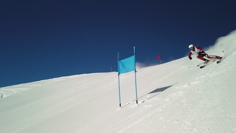 4K sport footage, professional skier in race suit with start number skiing on slope with giant slalom poles flags on sunny winter day with clear blue sky in slow motion
