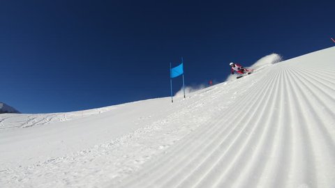 4K sport footage, professional skier in race suit with start number skiing on slope with giant slalom poles flags on sunny winter day with clear blue sky
