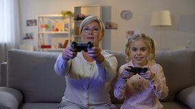 Cute girl and modern granny playing video game at home with joysticks, leisure