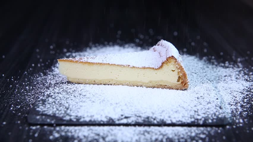 Pouring sugar on slice of cheesecake on stone plate close up shoot slow motion