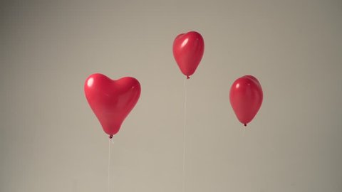 Three red heart shaped balloons floating in a studio