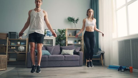 Young man and woman beautiful couple is jumping rope in house together doing sports indoors focused on practice. People, active lifestyle and relationship concept.