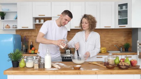 Young Smiling Couple Making Pancakes Together In The Kitchen In The Morning