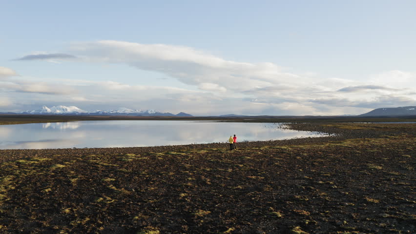 Aerial drone shot of a couple standing by a lake in interior of Iceland with mountains in background