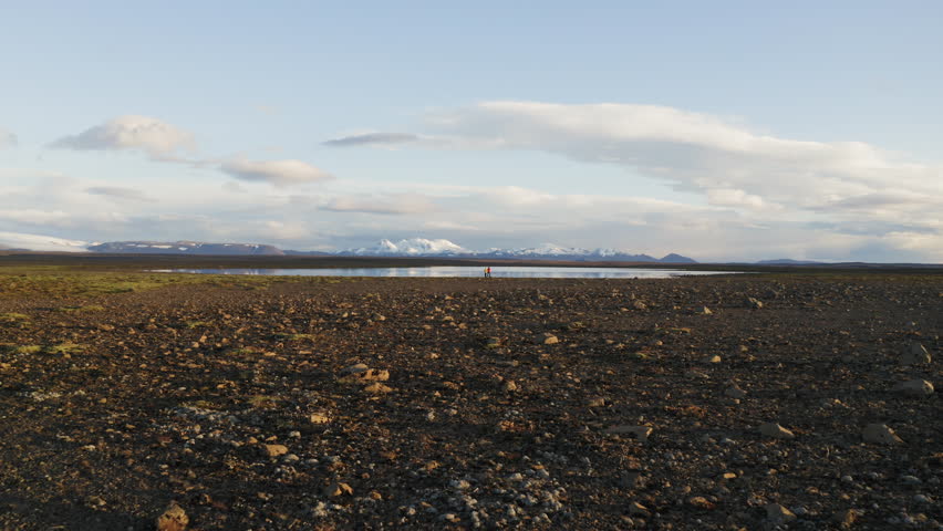 Aerial drone shot of a couple standing by a lake in interior of Iceland with mountains in background