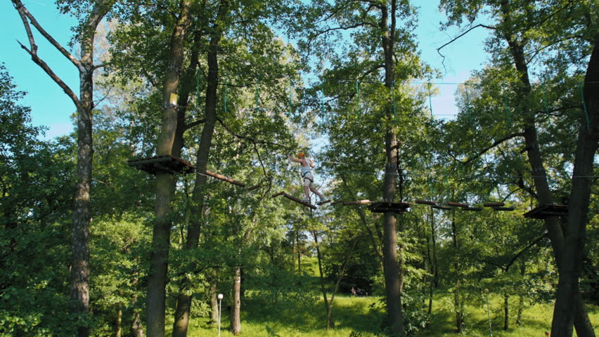 Man in Helmet in Adventure High Rope Park Doing Climbing Exercises on Balance Beam and Obstacle Course in Summer