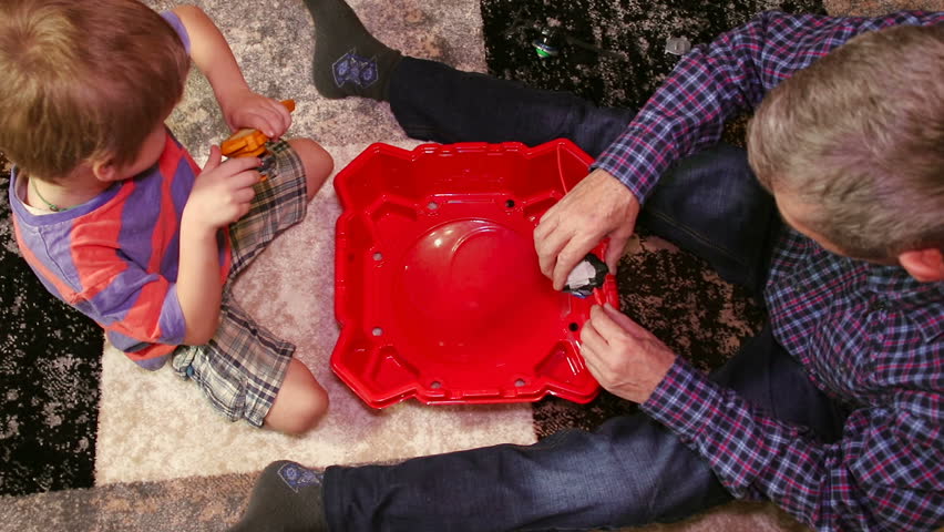Grandpa is playing with his grandson. Grandpa and his grandson have fun together. They sit on the floor in a room and play a game.
