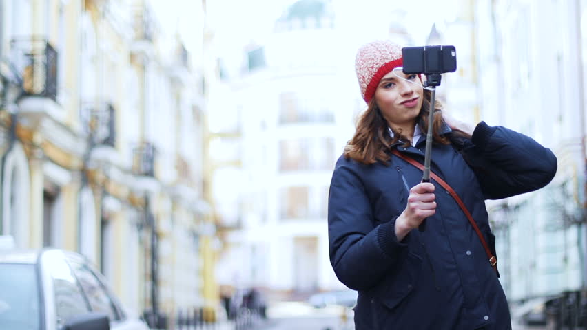 Young woman tourist taking selfie using smartphone, on the city street.