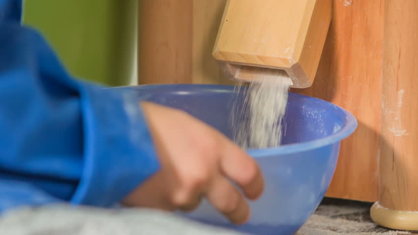 We can see how a flour is falling into a big blue container and a small boy is holding this container.