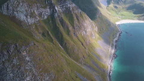 Aerial drone panning above Lofoten, Norway island and mountain range of tall cliff faces covered in lush green vegetation and blue water coastlines with low lying cloud during a picturesque sunset