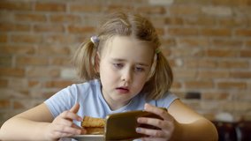 Girl using smartphone while eating a sandwich.