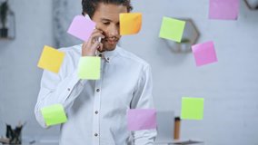 businessman talking on smartphone and checking information on colorful sticky notes