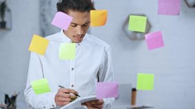 handsome businessman using digital tablet and writing on colorful sticky notes in office