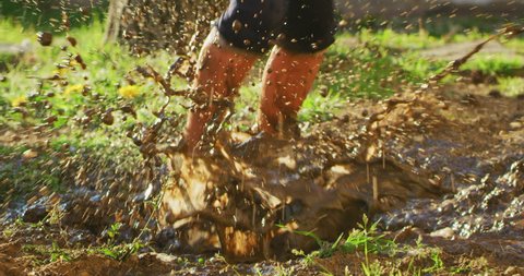 Authentic shot close up of barefoot little girl carefree having fun playing  and jumping in muddy puddle on a sunny day.