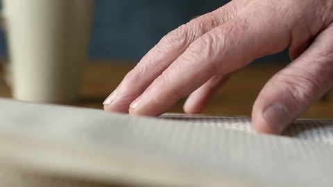 Handheld extreme close up shot of hand of elderly man touching page of book while reading novel
