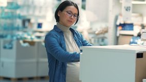 Happy pregnant Asian woman looking at cupboard in the market, Chinese pregnant woman choosing furniture in the supermarket, people consumption lifestyle 4k clip