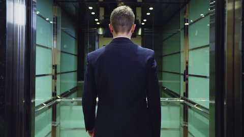 young well dressed businessman comes into modern elevator with large mirror and door closes slow motion backside view