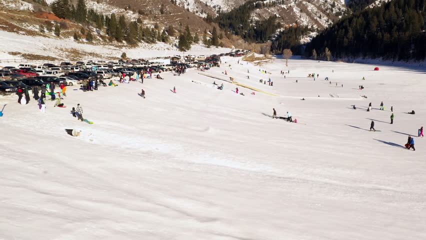People sledding down onto frozen lake in winter from small hill during the holidays on sunny day.