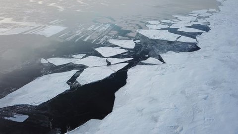 Aerial drone footage of ice on a frozen lake in sunset light.  Establishing shot for winter for climate change.