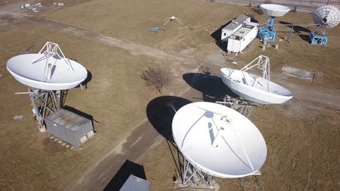 Aerial drone footage of an array of large satellite dishes or radio telescopes pointed skyward.