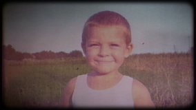 Family video archive. Retro camera 8 mm. Old film. Vintage. Portrait of a shy 4-year-old kid against a background of nature, the child looks into the camera and smiles, then looks away