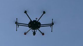 Ungraded: Hexacopter drone with a video camera hangs in the air against the blue sky. Bottom view. Ungraded H.264 from camera without re-encoding.