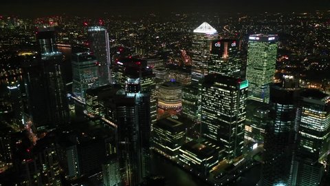 Docklands, London / United Kingdom - March 18 2019: Aerial bird's eye panoramic night video taken by drone of iconic Canary Wharf skyscraper complex and business district, Isle of dogs
