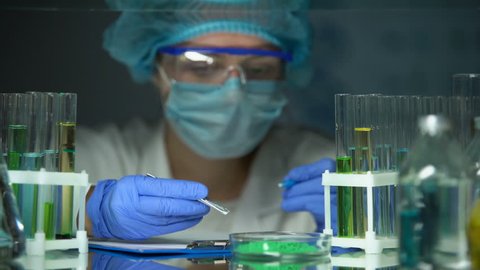 Left-handed researcher adding green powder to tube and making notes, experiment స్టాక్ వీడియో