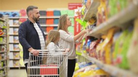 At the Supermarket: Happy Family of Three, Holding Hands, Walks Through Fresh Produce Section of the Store. Father Pushes Shopping Cart, Mother and Daughter Having Fun Time Shopping.