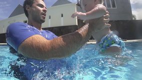Happy smiling newborn boy is diving under water with father in the swimming pool. Priceless health care for your baby. An underwater slowmotion video. Important to spend enough time with your kids