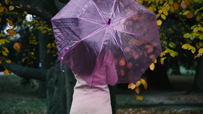 Young beautiful woman walking in the park on wet autumn day rotating a purple umbrella