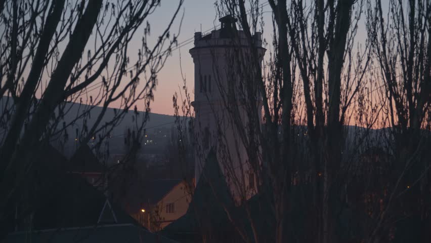 Big water tower behind the trees at sunset sky