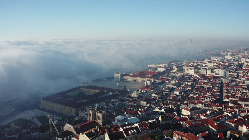 Aerial view; drone flight over Lisbon cityscape; panorama of Portuguese capital with main Commerce Square, Tagus river; morning fog; sunbeams shining and illuminated popular touristic routes of Lisboa Royalty-Free Stock Footage #1026398069
