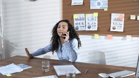 Young businesswoman talking on phone and then walking in the center of office, telling good news to team and start dancing with excitement; colleagues smiling, throwing up papers and taking pictures