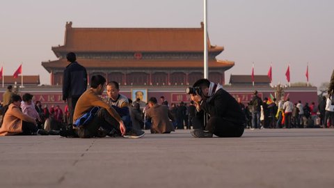 BEIJING - MARCH 23, 2018: Unidentified people sitting at at Tiananmen square against Gate of Heavenly Peace, man take pictures. Several of friends rest at city square of Beijing