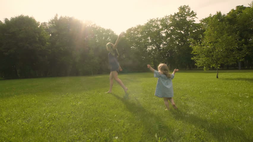 Baby girl with mother running through the grass in the summer sunlight in park. Baby have fun. Slow motion. Happy family concept. Child with mother running.