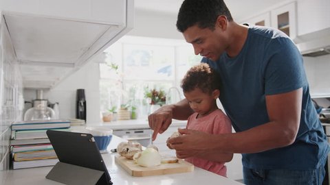 Millennial black father and toddler son preparing food together in the kitchen, side view, close up