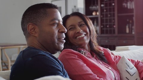Close up of black middle aged couple sitting on the sofa in their living room watching TV together Stockvideo