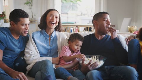 Three generation mixed race family sitting on the sofa watching TV and eating popcorn, panning shot