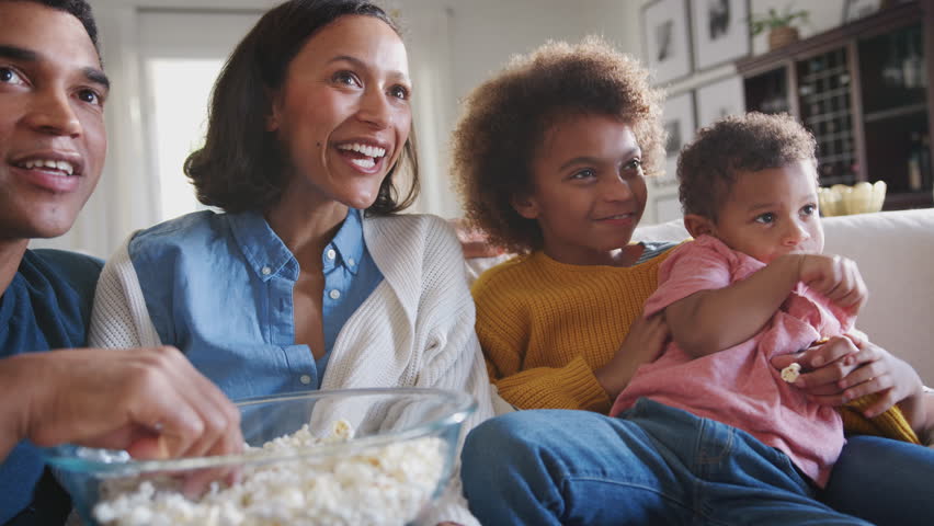 Young mixed race family sitting on the sofa watching TV and eating popcorn, low angle, close up Royalty-Free Stock Footage #1026410861
