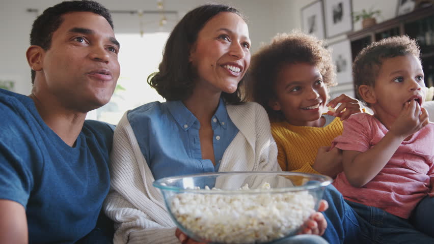 Young mixed race family sitting on the sofa watching TV and eating popcorn, low angle, close up Royalty-Free Stock Footage #1026410861