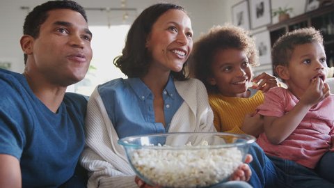 Young mixed race family sitting on the sofa watching TV and eating popcorn, low angle, close up