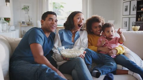 Young mixed race family sitting on the sofa at home watching TV and eating popcorn