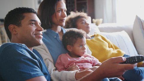 Young family sitting together on the sofa in their living room watching TV, close up, side view