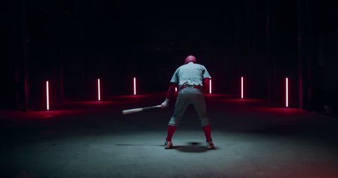 WIDE FIXED Caucasian professional baseball player batter hitting a ball against dark background. 4K UHD 60 FPS SLOW MOTION