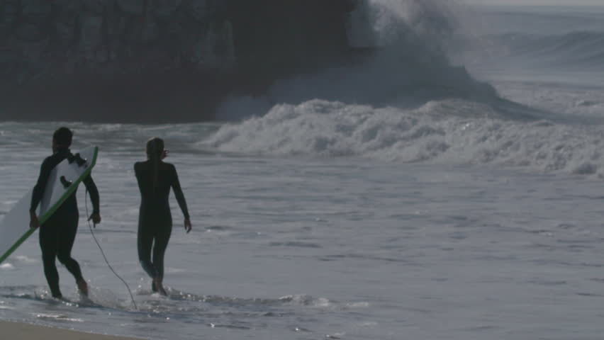 Two persons walking on a beach with a surfboard, Atlantic Ocean, Hossegor, France - Slow motion