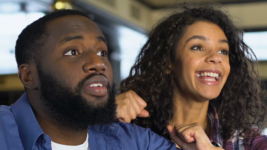 Black couple happy about favorite sports team victory, watching game in pub