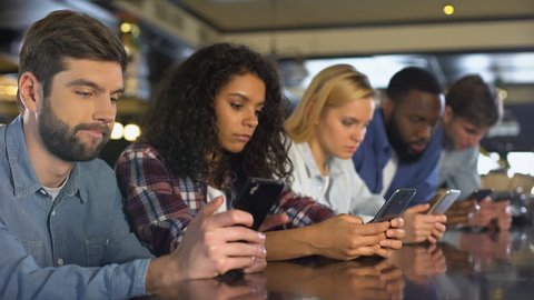 Multi-racial friends scrolling smartphones ignoring each other, gadget addiction